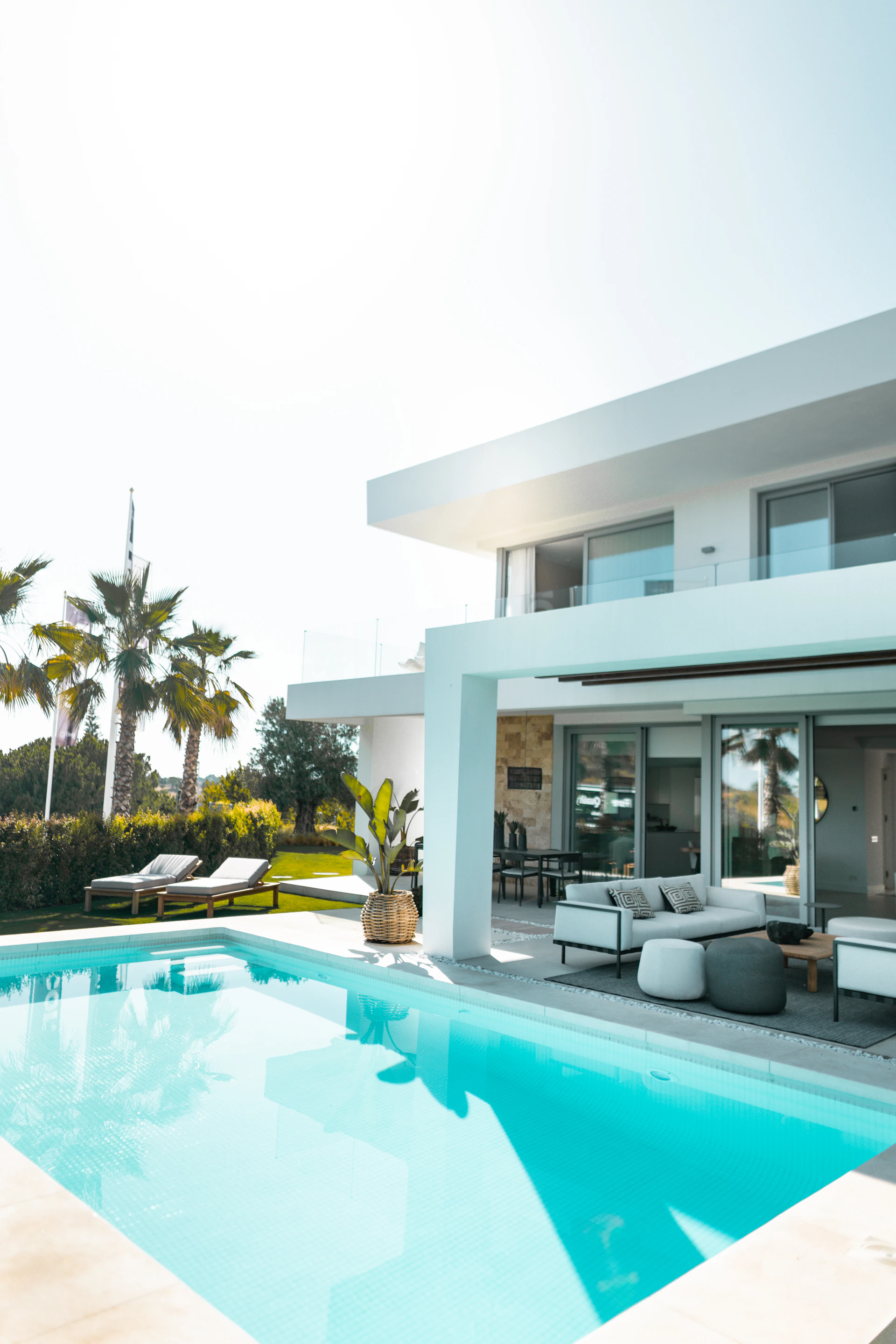 White contemporary house with glass doors, a shaded terrace and a turquoise swimming pool